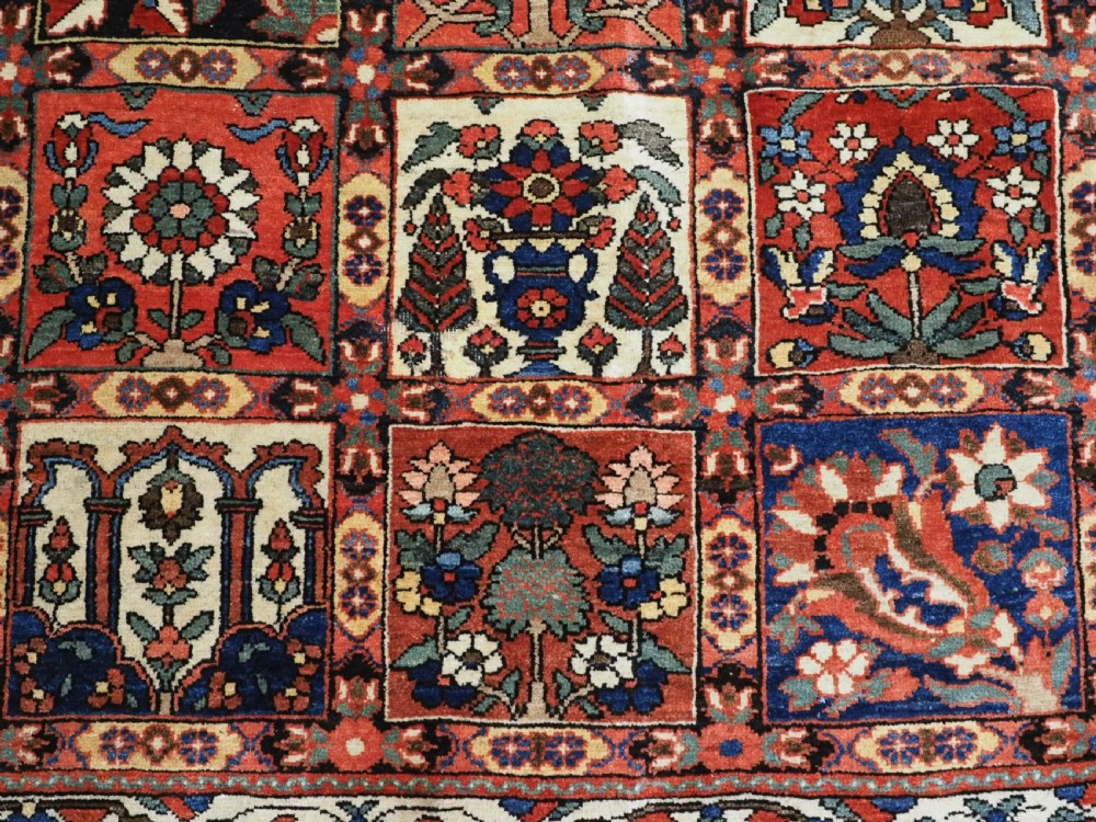 A large antique Bakhtiari wool carpet featuring a repeating grid pattern of garden motifs in terracotta red, navy blue, and ivory framed by a wide ornamental border. View XI