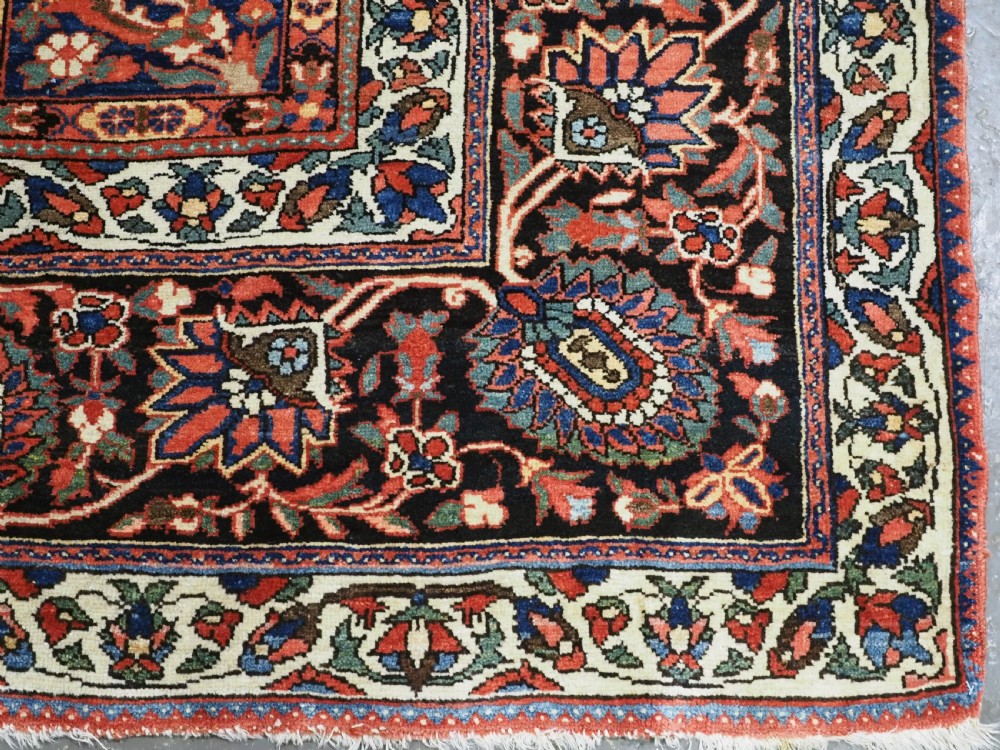 A large antique Bakhtiari wool carpet featuring a repeating grid pattern of garden motifs in terracotta red, navy blue, and ivory framed by a wide ornamental border. View XIII