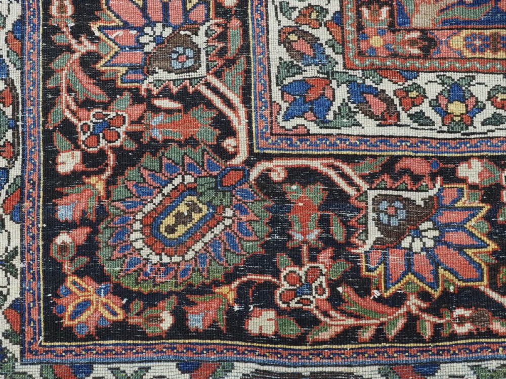 A large antique Bakhtiari wool carpet featuring a repeating grid pattern of garden motifs in terracotta red, navy blue, and ivory framed by a wide ornamental border. View XIV
