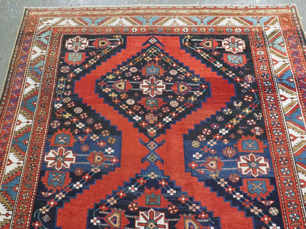 An antique Caucasian Kazak kelleh rug with a central red field, blue geometric diamond medallions, and multi-layered patterned borders. View III