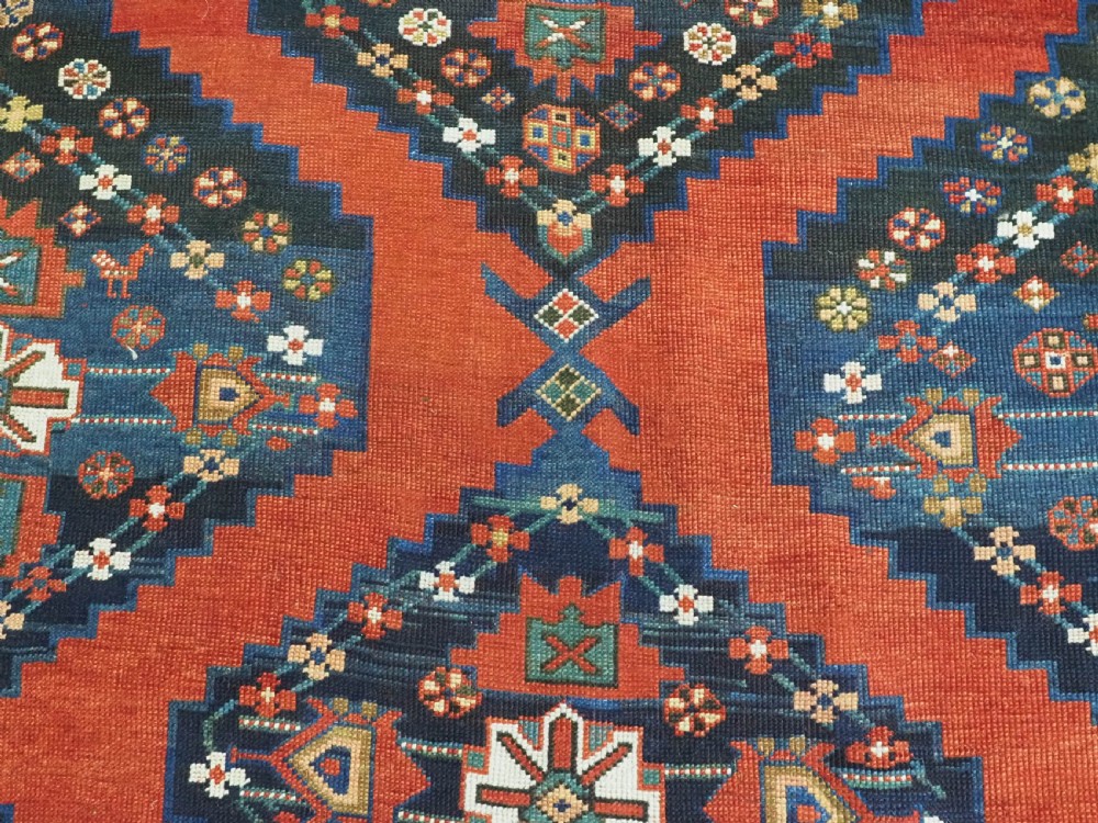 An antique Caucasian Kazak kelleh rug with a central red field, blue geometric diamond medallions, and multi-layered patterned borders. View XI