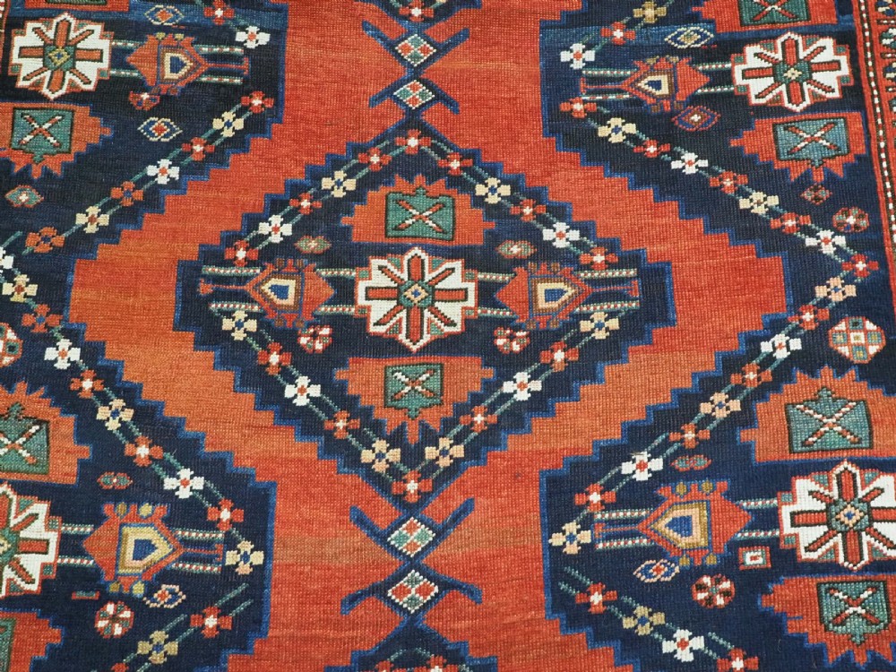An antique Caucasian Kazak kelleh rug with a central red field, blue geometric diamond medallions, and multi-layered patterned borders. View XII