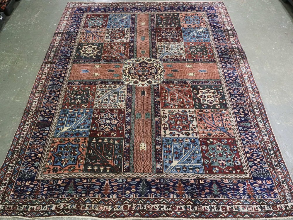 A rectangular hand-knotted wool carpet featuring a central grid of garden panels framed by a wide dark navy geometric border in terracotta, blue, and cream tones.