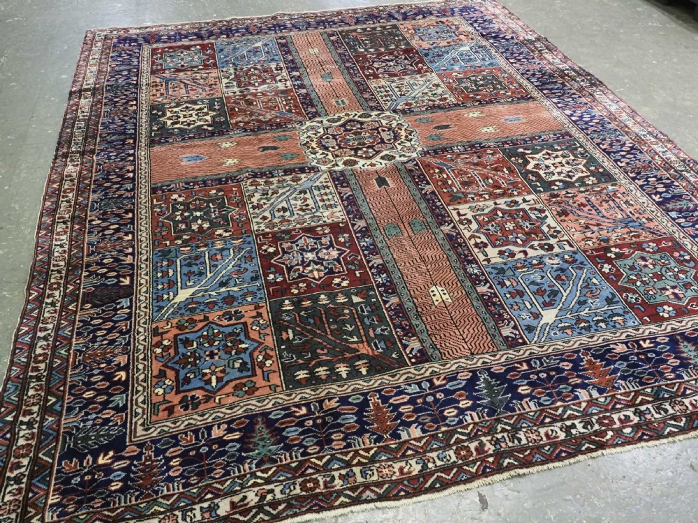 A rectangular hand-knotted wool carpet featuring a central grid of garden panels framed by a wide dark navy geometric border in terracotta, blue, and cream tones. View II
