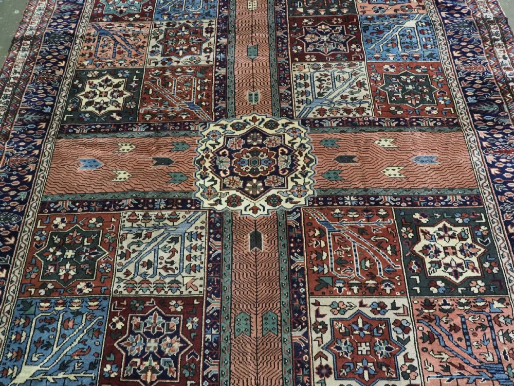 A rectangular hand-knotted wool carpet featuring a central grid of garden panels framed by a wide dark navy geometric border in terracotta, blue, and cream tones. View IV
