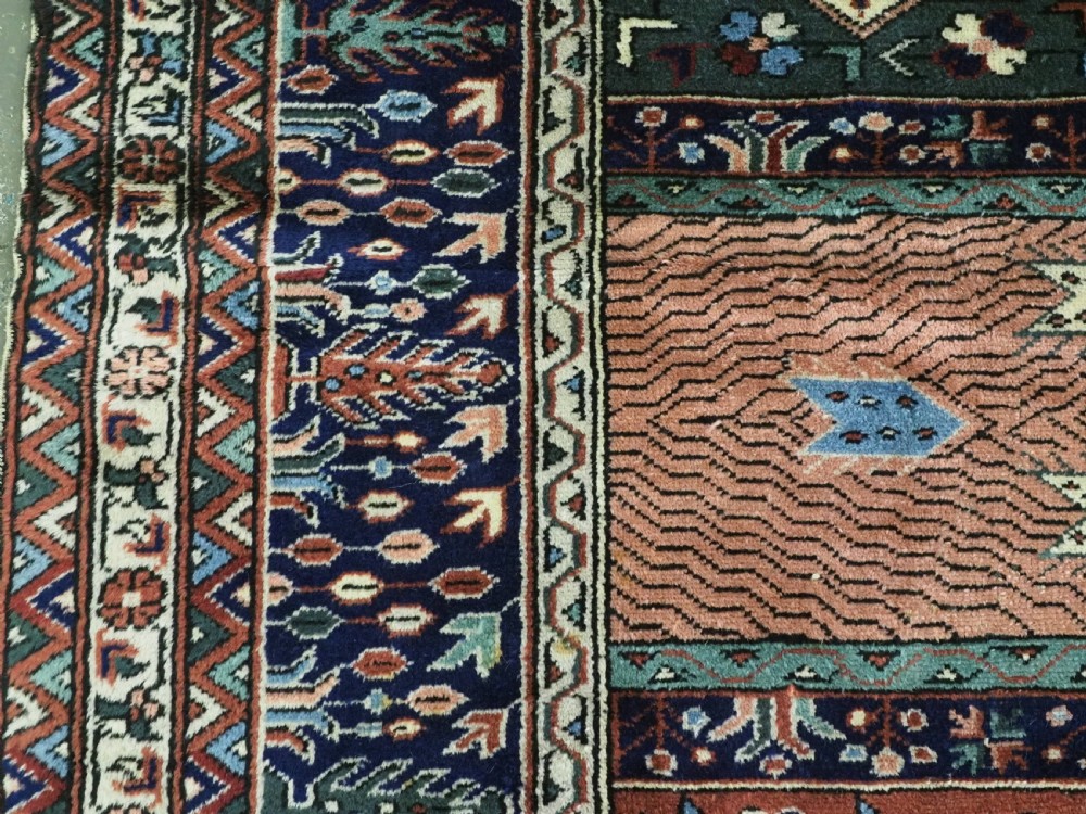 A rectangular hand-knotted wool carpet featuring a central grid of garden panels framed by a wide dark navy geometric border in terracotta, blue, and cream tones. View VII