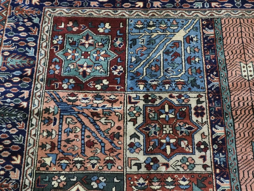 A rectangular hand-knotted wool carpet featuring a central grid of garden panels framed by a wide dark navy geometric border in terracotta, blue, and cream tones. View VIII