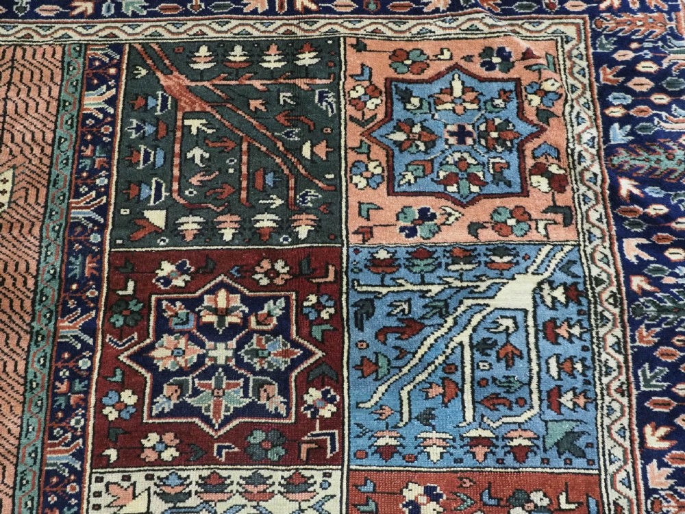 A rectangular hand-knotted wool carpet featuring a central grid of garden panels framed by a wide dark navy geometric border in terracotta, blue, and cream tones. View IX