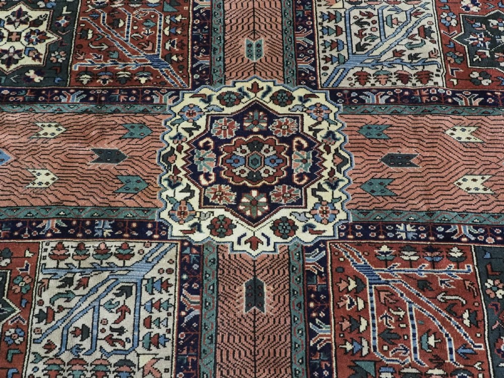 A rectangular hand-knotted wool carpet featuring a central grid of garden panels framed by a wide dark navy geometric border in terracotta, blue, and cream tones. View X