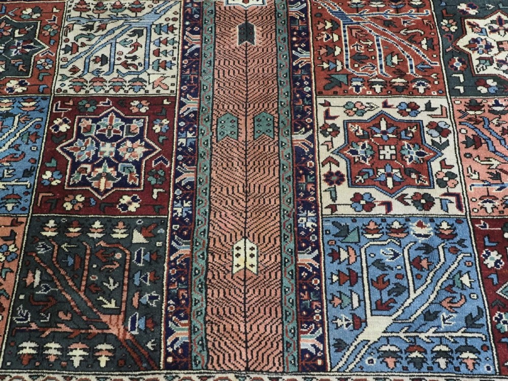 A rectangular hand-knotted wool carpet featuring a central grid of garden panels framed by a wide dark navy geometric border in terracotta, blue, and cream tones. View XI