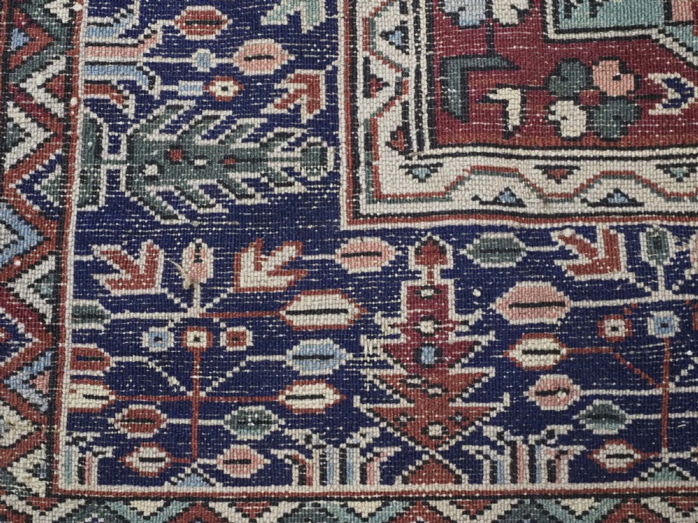 A rectangular hand-knotted wool carpet featuring a central grid of garden panels framed by a wide dark navy geometric border in terracotta, blue, and cream tones. View XIII