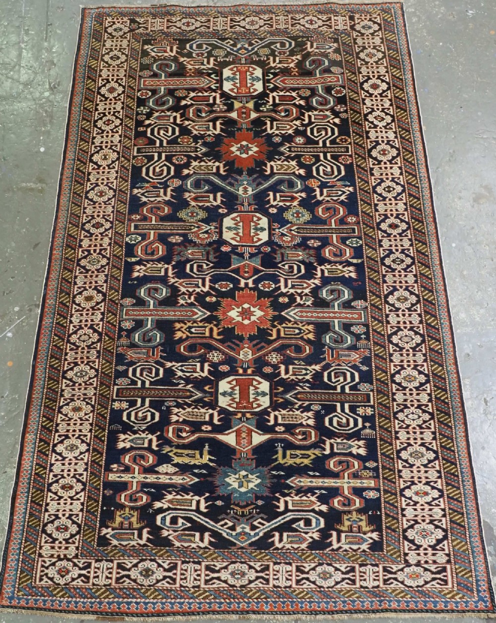 An antique hand-knotted Caucasian Perepedil rug featuring a navy blue field with geometric rams horn motifs and star medallions framed by multi-layered geometric borders.