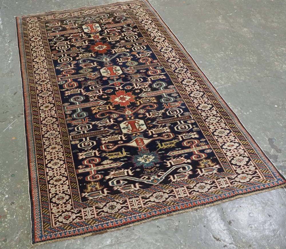 An antique hand-knotted Caucasian Perepedil rug featuring a navy blue field with geometric rams horn motifs and star medallions framed by multi-layered geometric borders. View II