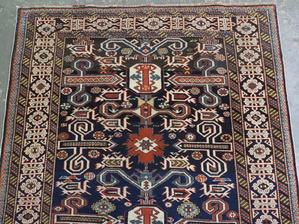 An antique hand-knotted Caucasian Perepedil rug featuring a navy blue field with geometric rams horn motifs and star medallions framed by multi-layered geometric borders. View III