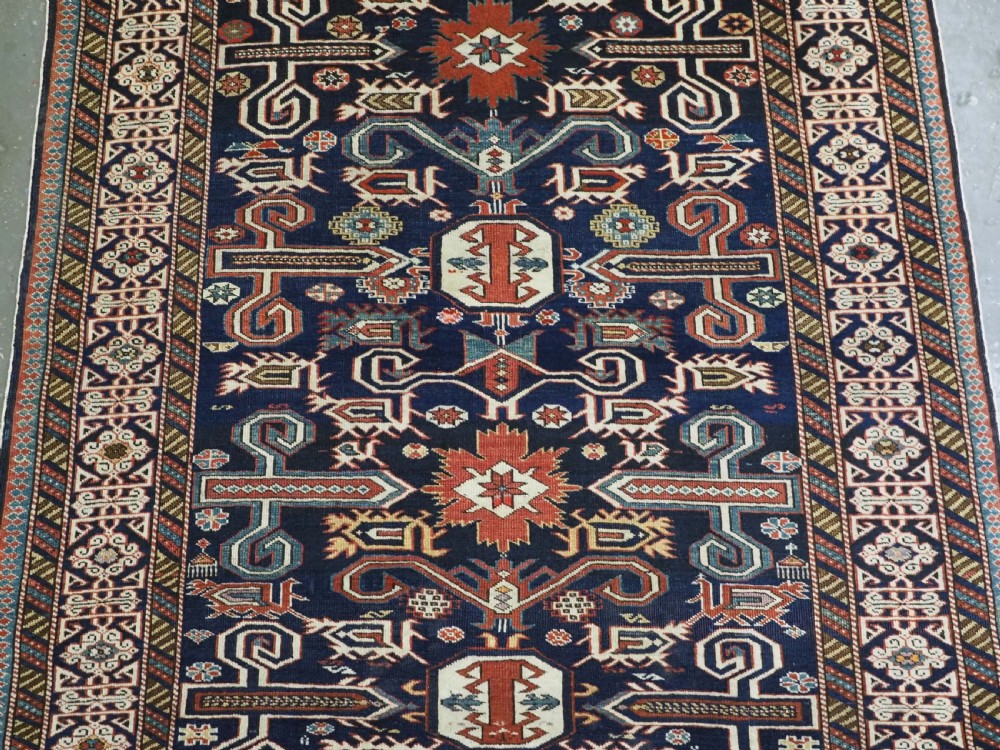 An antique hand-knotted Caucasian Perepedil rug featuring a navy blue field with geometric rams horn motifs and star medallions framed by multi-layered geometric borders. View IV