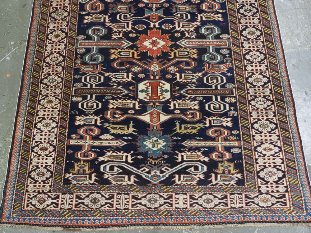 An antique hand-knotted Caucasian Perepedil rug featuring a navy blue field with geometric rams horn motifs and star medallions framed by multi-layered geometric borders. View V