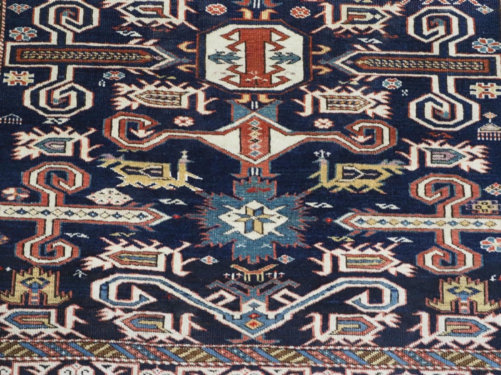 An antique hand-knotted Caucasian Perepedil rug featuring a navy blue field with geometric rams horn motifs and star medallions framed by multi-layered geometric borders. View X