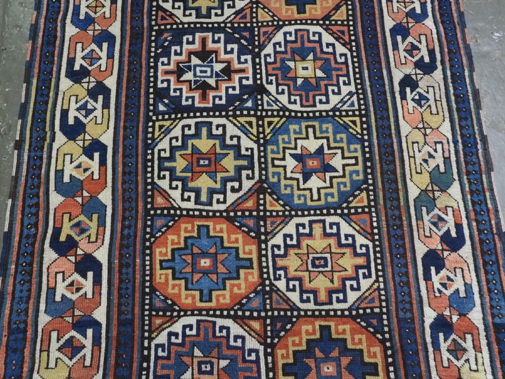 An antique Caucasian Moghan Kazak hand-knotted wool runner rug featuring a repeating geometric Memling gul pattern in navy, terracotta, ochre, and cream. View IV