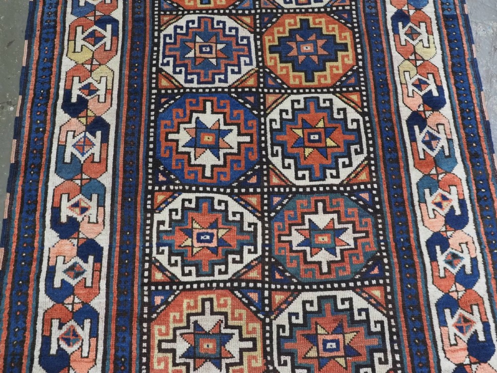 An antique Caucasian Moghan Kazak hand-knotted wool runner rug featuring a repeating geometric Memling gul pattern in navy, terracotta, ochre, and cream. View V