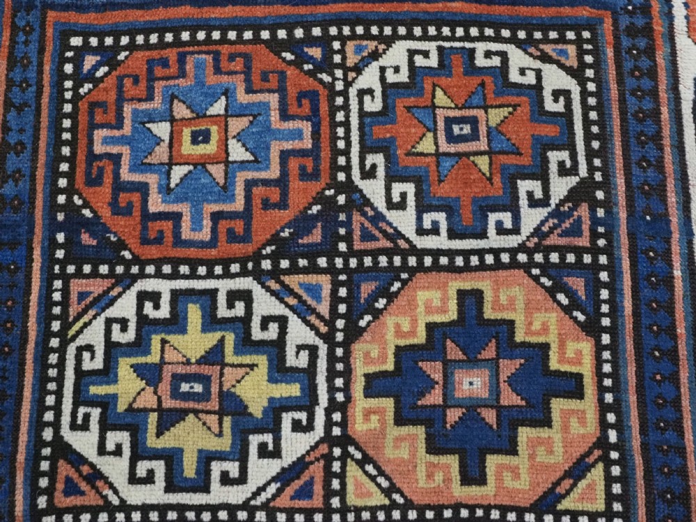 An antique Caucasian Moghan Kazak hand-knotted wool runner rug featuring a repeating geometric Memling gul pattern in navy, terracotta, ochre, and cream. View IX