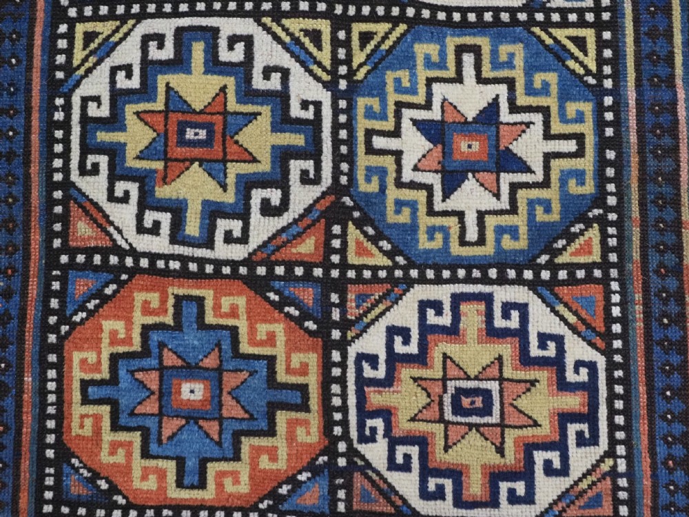 An antique Caucasian Moghan Kazak hand-knotted wool runner rug featuring a repeating geometric Memling gul pattern in navy, terracotta, ochre, and cream. View X