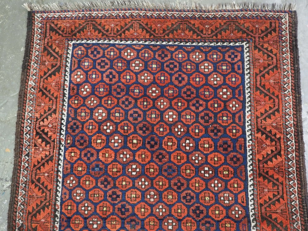 An antique hand-knotted Baluch rug featuring a navy blue central field filled with a repeat pattern of rust red octagons inside a geometric border. View III