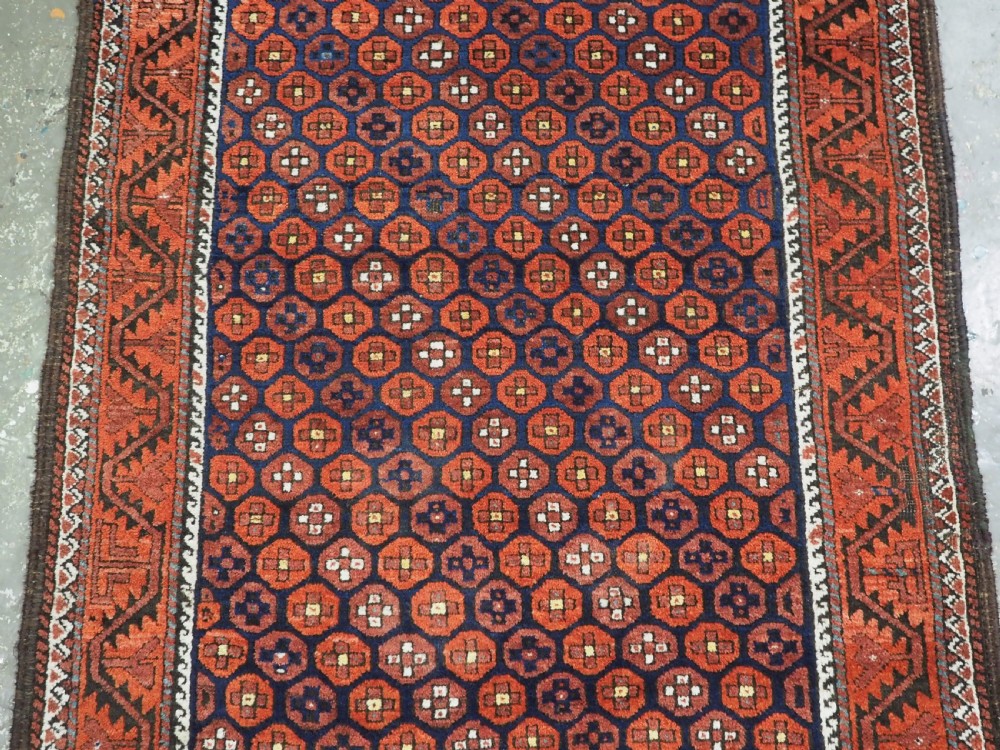 An antique hand-knotted Baluch rug featuring a navy blue central field filled with a repeat pattern of rust red octagons inside a geometric border. View IV