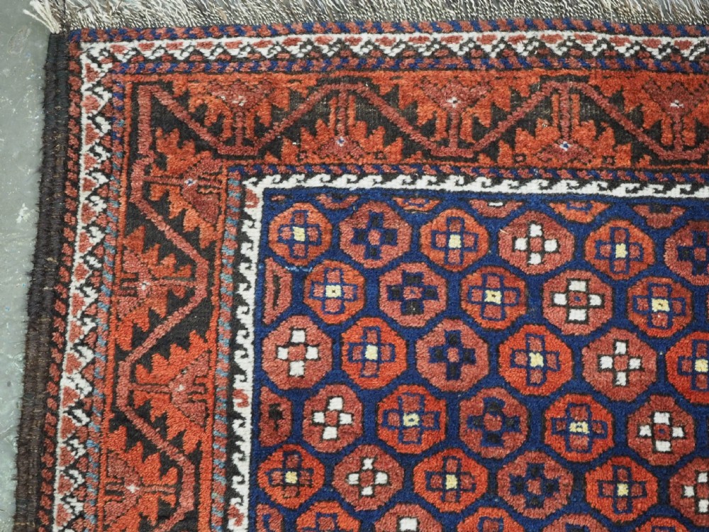 An antique hand-knotted Baluch rug featuring a navy blue central field filled with a repeat pattern of rust red octagons inside a geometric border. View V