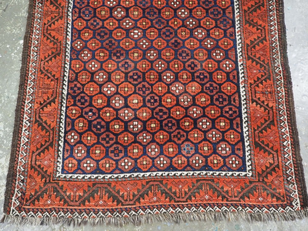 An antique hand-knotted Baluch rug featuring a navy blue central field filled with a repeat pattern of rust red octagons inside a geometric border. View VI