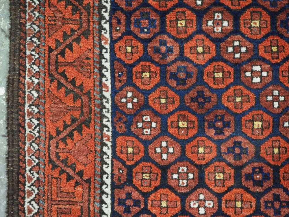 An antique hand-knotted Baluch rug featuring a navy blue central field filled with a repeat pattern of rust red octagons inside a geometric border. View VII