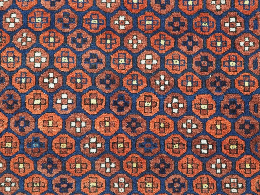 An antique hand-knotted Baluch rug featuring a navy blue central field filled with a repeat pattern of rust red octagons inside a geometric border. View VIII
