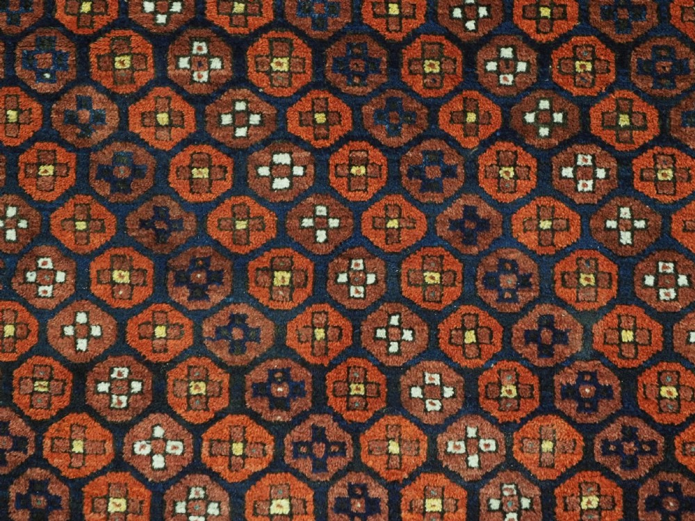 An antique hand-knotted Baluch rug featuring a navy blue central field filled with a repeat pattern of rust red octagons inside a geometric border. View IX