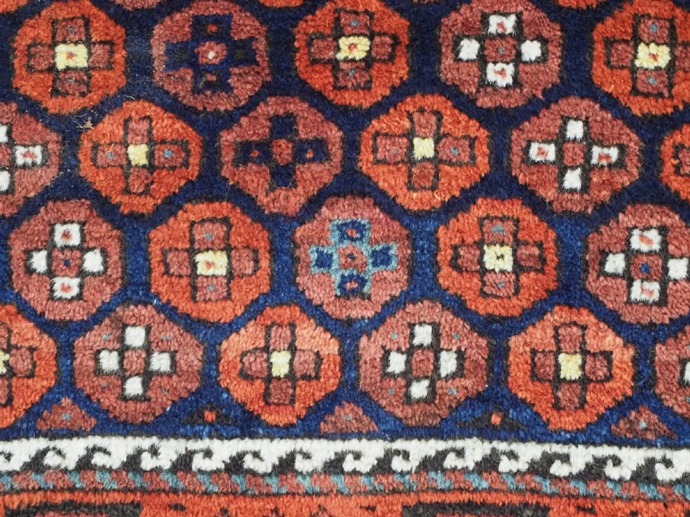 An antique hand-knotted Baluch rug featuring a navy blue central field filled with a repeat pattern of rust red octagons inside a geometric border. View X