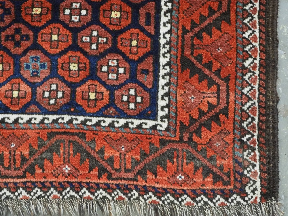 An antique hand-knotted Baluch rug featuring a navy blue central field filled with a repeat pattern of rust red octagons inside a geometric border. View XI