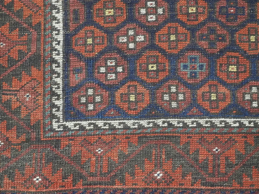 An antique hand-knotted Baluch rug featuring a navy blue central field filled with a repeat pattern of rust red octagons inside a geometric border. View XII