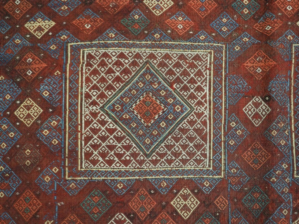 An antique Caucasian flatweave rug displaying geometric diamond medallions in rust red, navy blue, and cream wool with fringed ends. View VIII