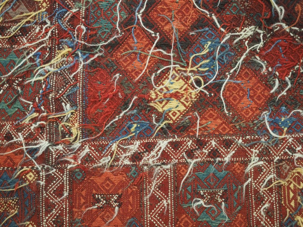 An antique Caucasian flatweave rug displaying geometric diamond medallions in rust red, navy blue, and cream wool with fringed ends. View XIV