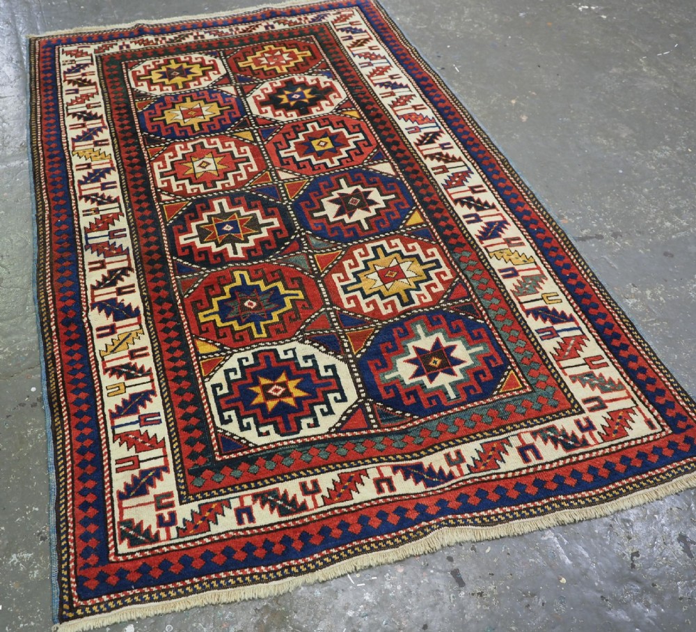 An antique Caucasian Moghan Kazak hand-knotted wool rug featuring two vertical columns of geometric Memling guls inside a multi-tiered border. View II