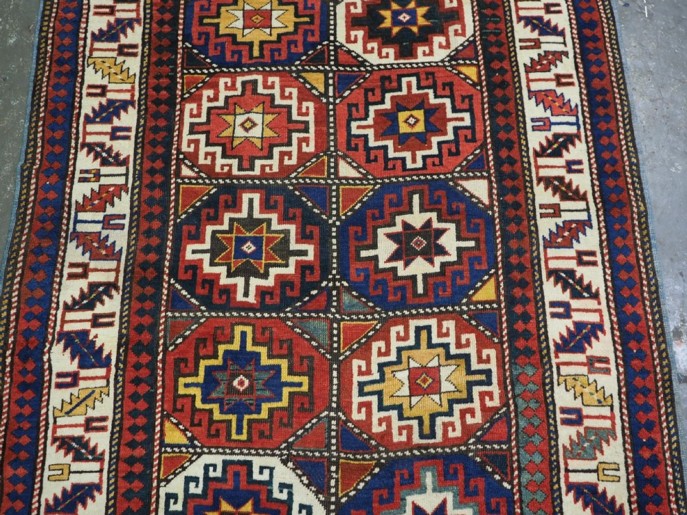 An antique Caucasian Moghan Kazak hand-knotted wool rug featuring two vertical columns of geometric Memling guls inside a multi-tiered border. View IV
