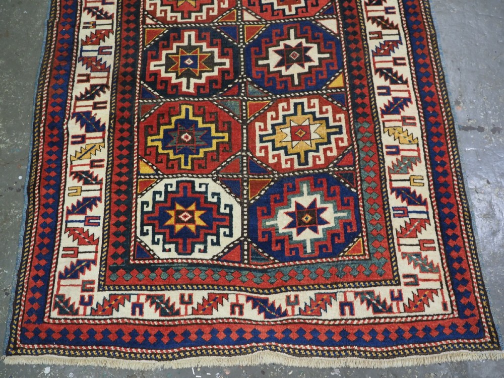 An antique Caucasian Moghan Kazak hand-knotted wool rug featuring two vertical columns of geometric Memling guls inside a multi-tiered border. View V