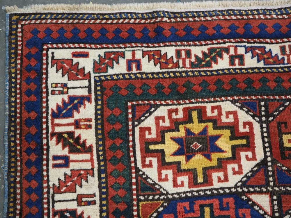 An antique Caucasian Moghan Kazak hand-knotted wool rug featuring two vertical columns of geometric Memling guls inside a multi-tiered border. View VI