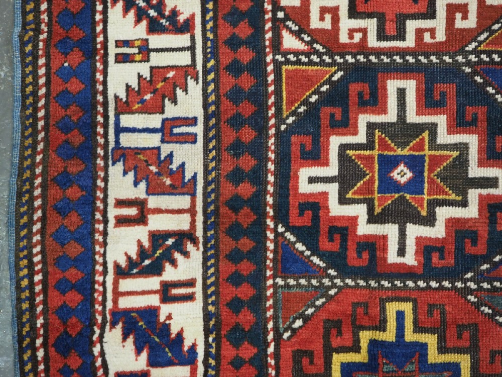 An antique Caucasian Moghan Kazak hand-knotted wool rug featuring two vertical columns of geometric Memling guls inside a multi-tiered border. View VII