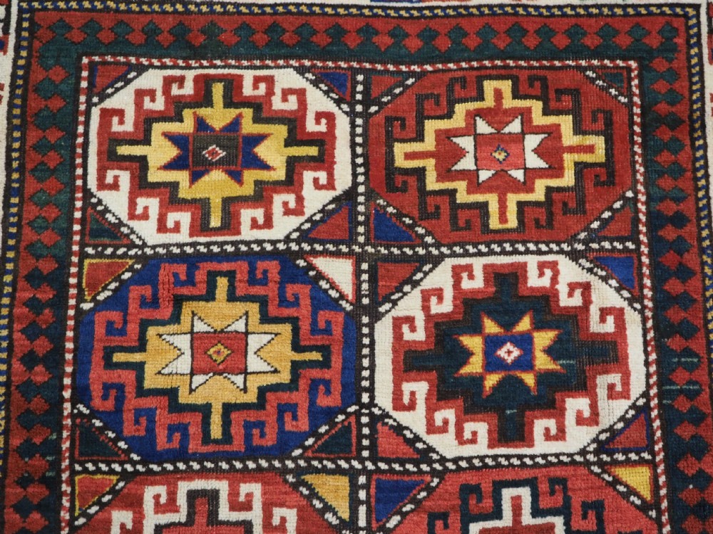 An antique Caucasian Moghan Kazak hand-knotted wool rug featuring two vertical columns of geometric Memling guls inside a multi-tiered border. View VIII