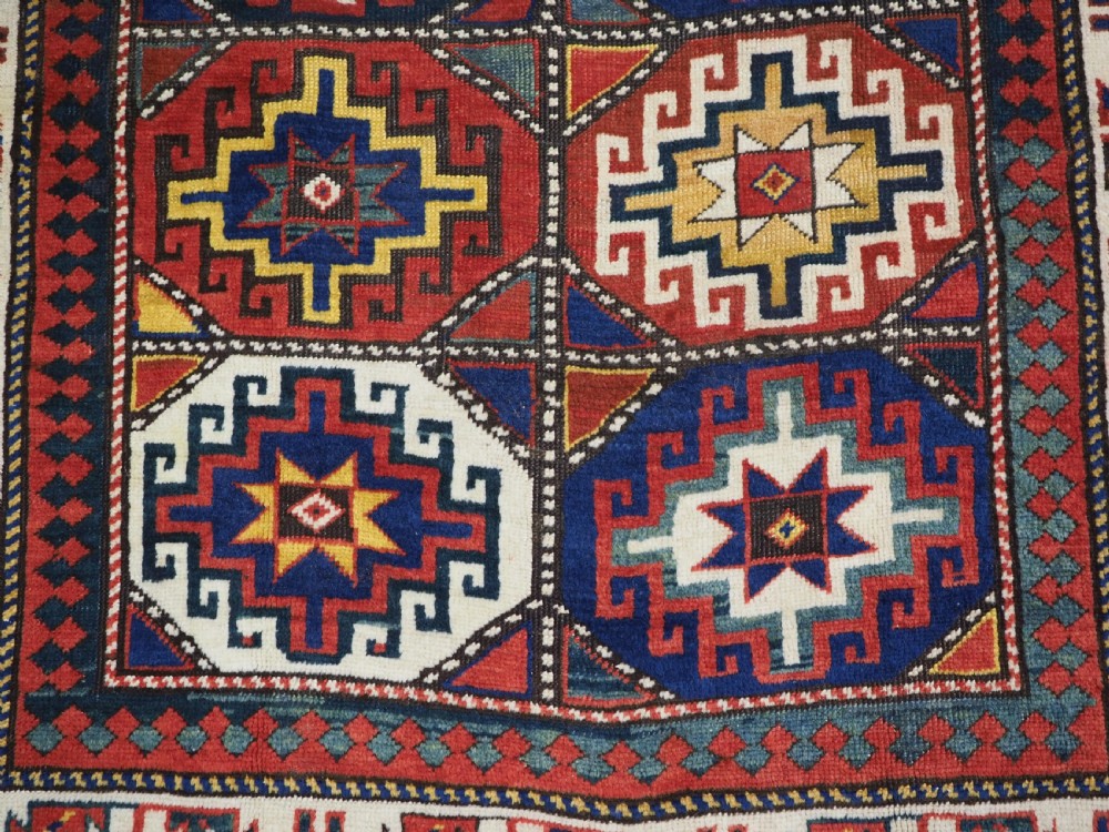 An antique Caucasian Moghan Kazak hand-knotted wool rug featuring two vertical columns of geometric Memling guls inside a multi-tiered border. View IX