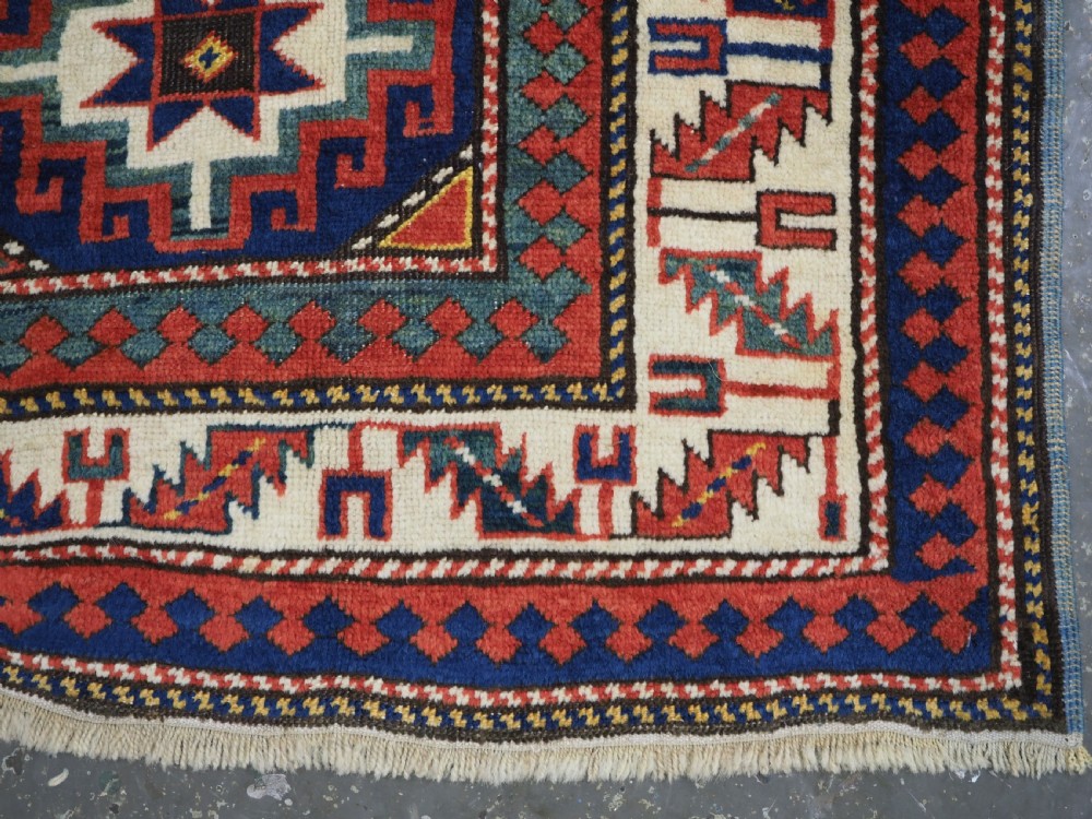 An antique Caucasian Moghan Kazak hand-knotted wool rug featuring two vertical columns of geometric Memling guls inside a multi-tiered border. View X