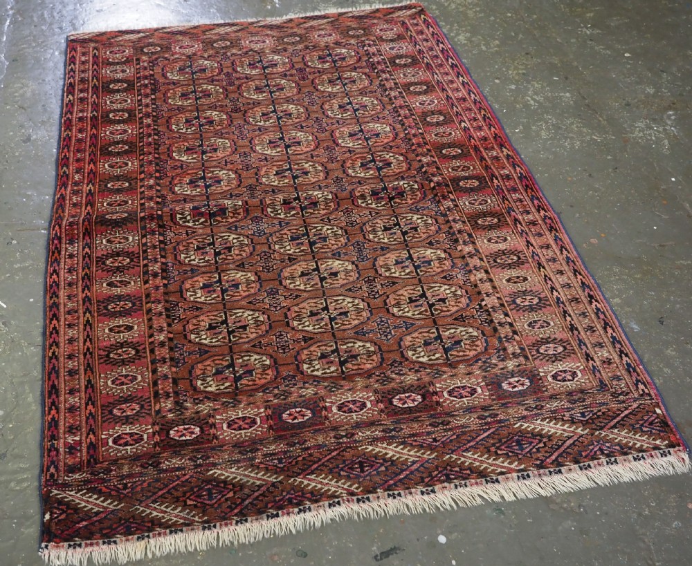 An antique rectangular hand-knotted wool Tekke Turkmen rug featuring repeating octagonal gul motifs in terracotta, navy, and cream tones with geometric borders. View II