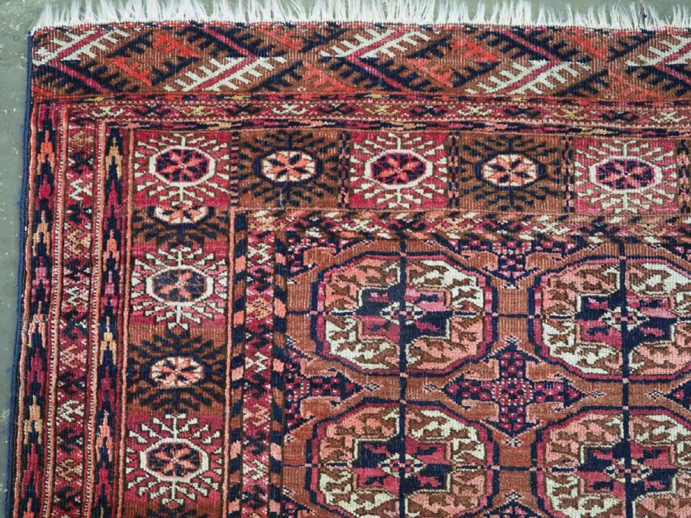 An antique rectangular hand-knotted wool Tekke Turkmen rug featuring repeating octagonal gul motifs in terracotta, navy, and cream tones with geometric borders. View V