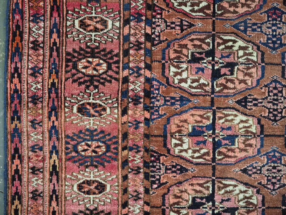 An antique rectangular hand-knotted wool Tekke Turkmen rug featuring repeating octagonal gul motifs in terracotta, navy, and cream tones with geometric borders. View VI