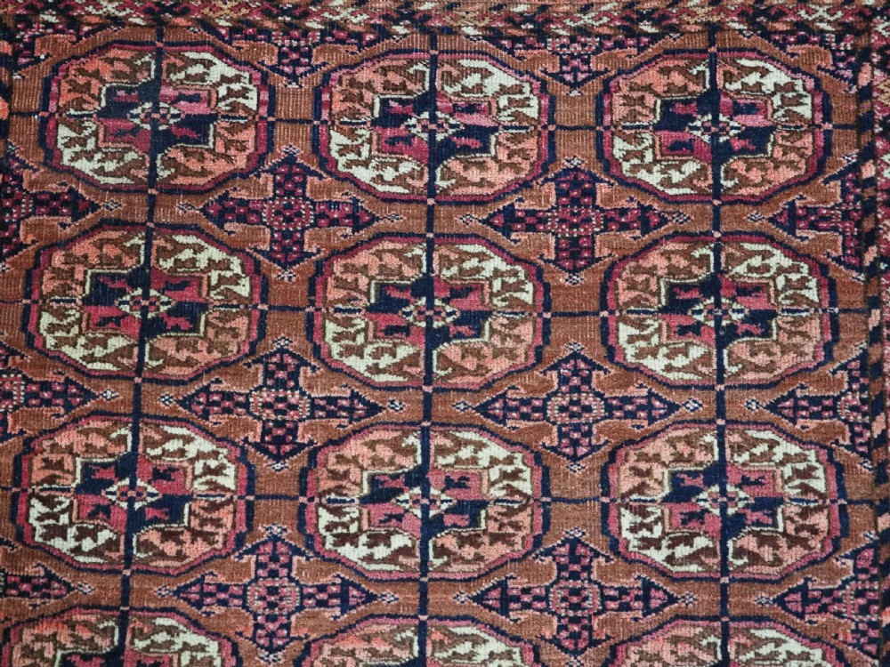 An antique rectangular hand-knotted wool Tekke Turkmen rug featuring repeating octagonal gul motifs in terracotta, navy, and cream tones with geometric borders. View VII
