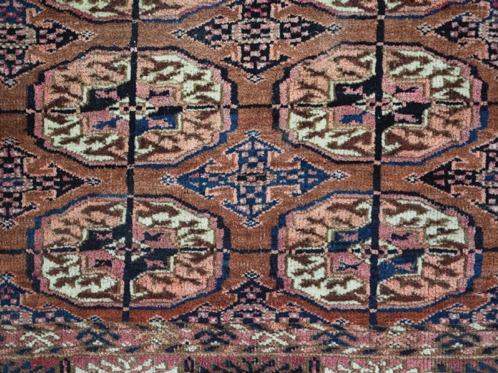 An antique rectangular hand-knotted wool Tekke Turkmen rug featuring repeating octagonal gul motifs in terracotta, navy, and cream tones with geometric borders. View VIII
